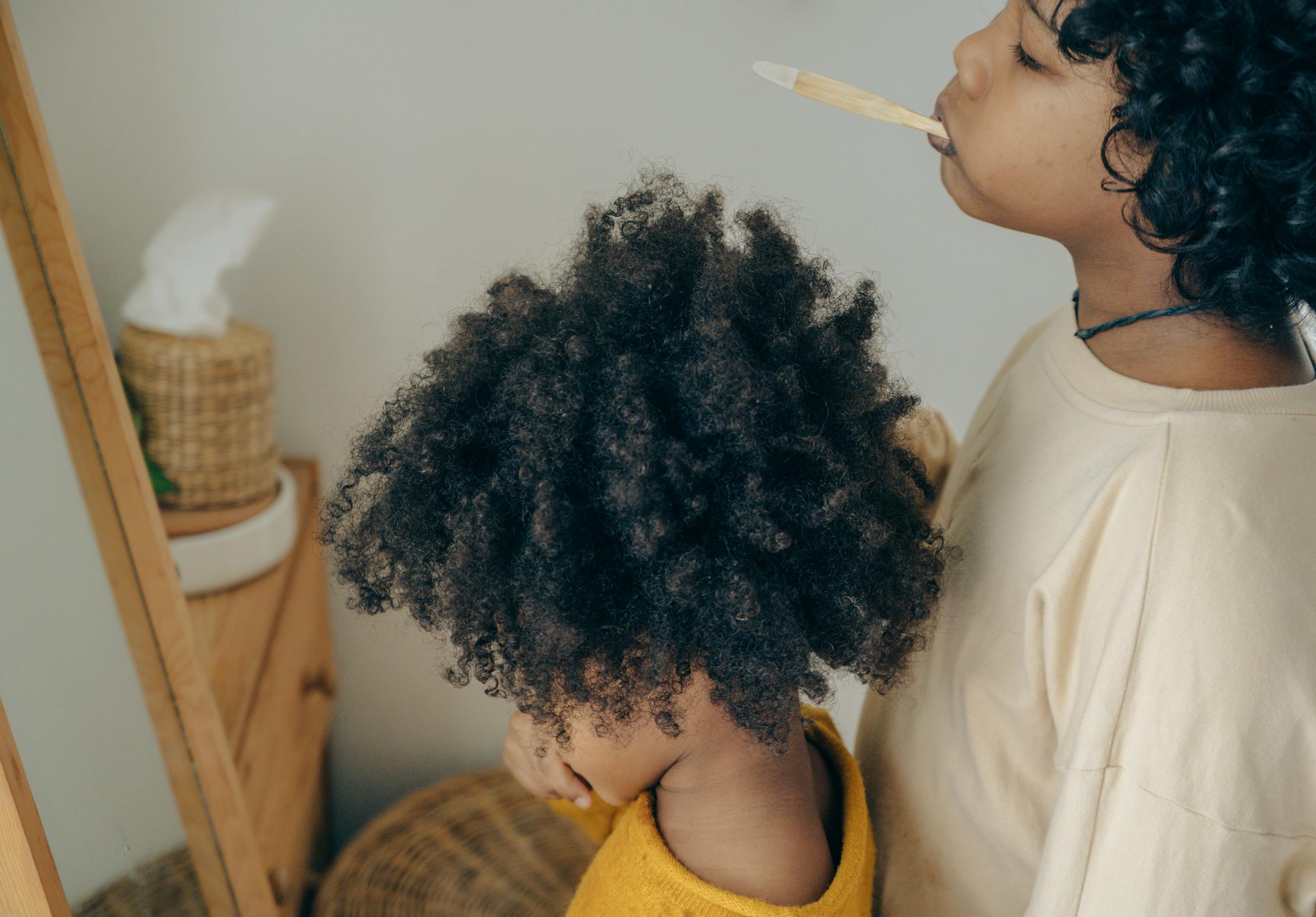 From above side view of ethnic children in casual outfit brushing teeth together in front of mirror in cozy bathroom